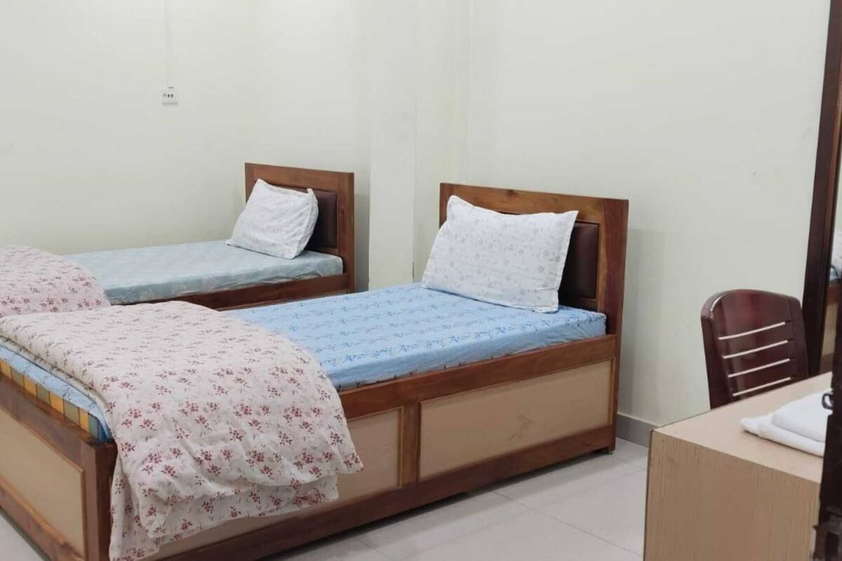 Une pièce avec deux lits en bois, chacun étant muni d’un oreiller et d’une couverture. On y trouve également une chaise en bois et une petite table sur laquelle est posée une serviette.