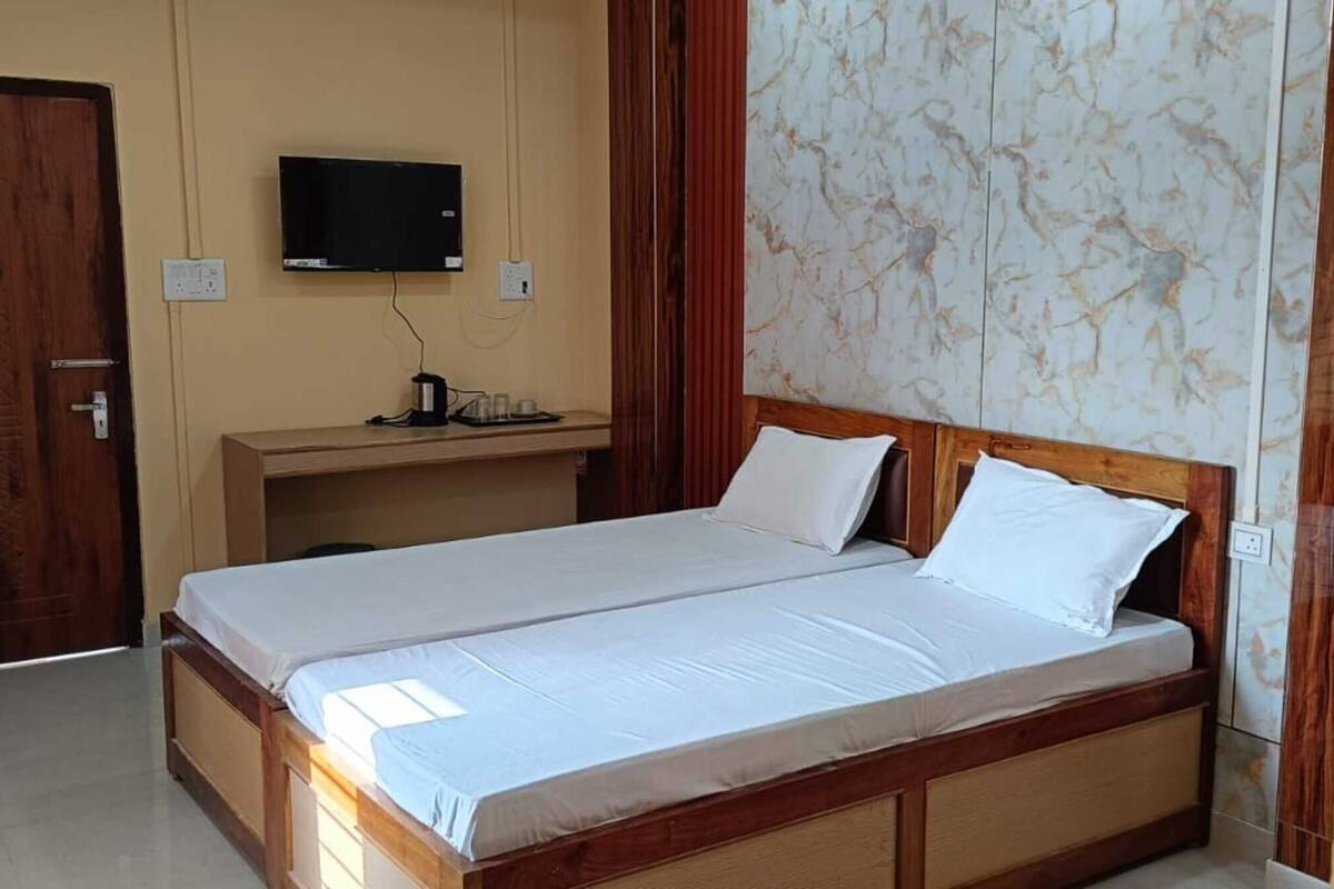 Une chambre avec un lit en bois, un bureau avec une télévision et un mur décoré d’un motif imitant le marbre.