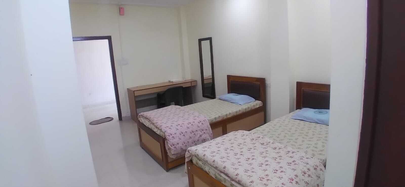 A room with two single beds, a desk, a chair, and a mirror.