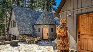 Una cabaña con patio de piedra, muebles de madera y una escultura de oso.