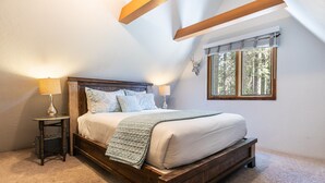 Un dormitorio con cama de madera, dos lámparas de noche, un ventanal con persianas y una mesita con lámpara.