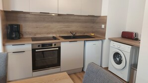 Une cuisine compacte équipée d’une machine à café, d’un four, d’un lave-vaisselle et d’un lave-linge.