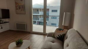 Un salon comprenant un canapé, une petite table avec une plante, un téléviseur et une porte-fenêtre coulissante donnant sur un balcon.