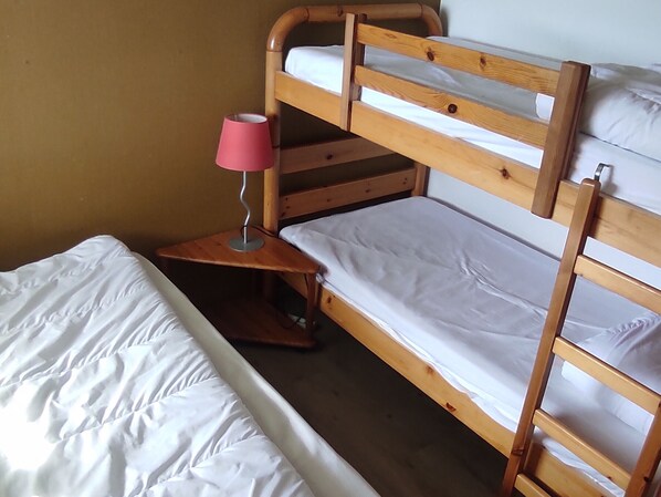 Un lit superposé avec une structure en bois, une table de chevet avec une lampe et un matelas blanc.
