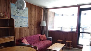 A room with a wooden interior, a red patterned sofa, a wooden table, and a window with a view.