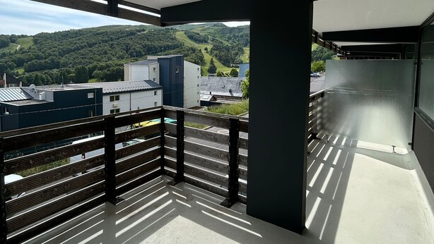 A balcony with a view of a green hillside and buildings.