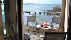 A balcony with a table set for two, overlooking a body of water and a distant shoreline. - Seaside apartment with balcony, private parking in Les Sables-d'Olonne (Les Sables-d'Olonne)