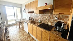 A kitchen with wooden cabinets, a black stove, and a tiled backsplash. - Seaside apartment with balcony, private parking in Les Sables-d'Olonne (Les Sables-d'Olonne)