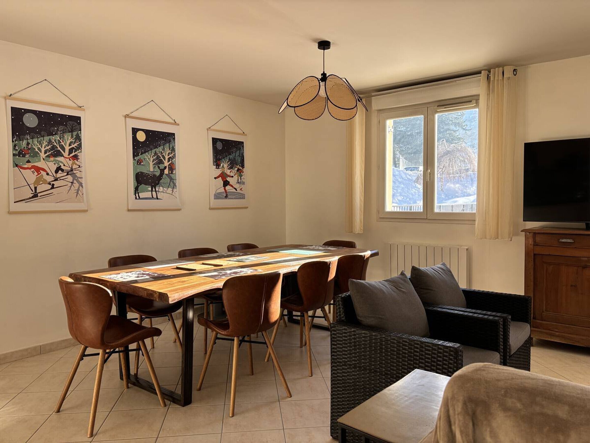 A dining area with a long table, chairs, a television, and artwork on the walls.