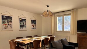 Una zona de menjador amb una taula llarga, cadires, televisió i obres d'art a les parets.