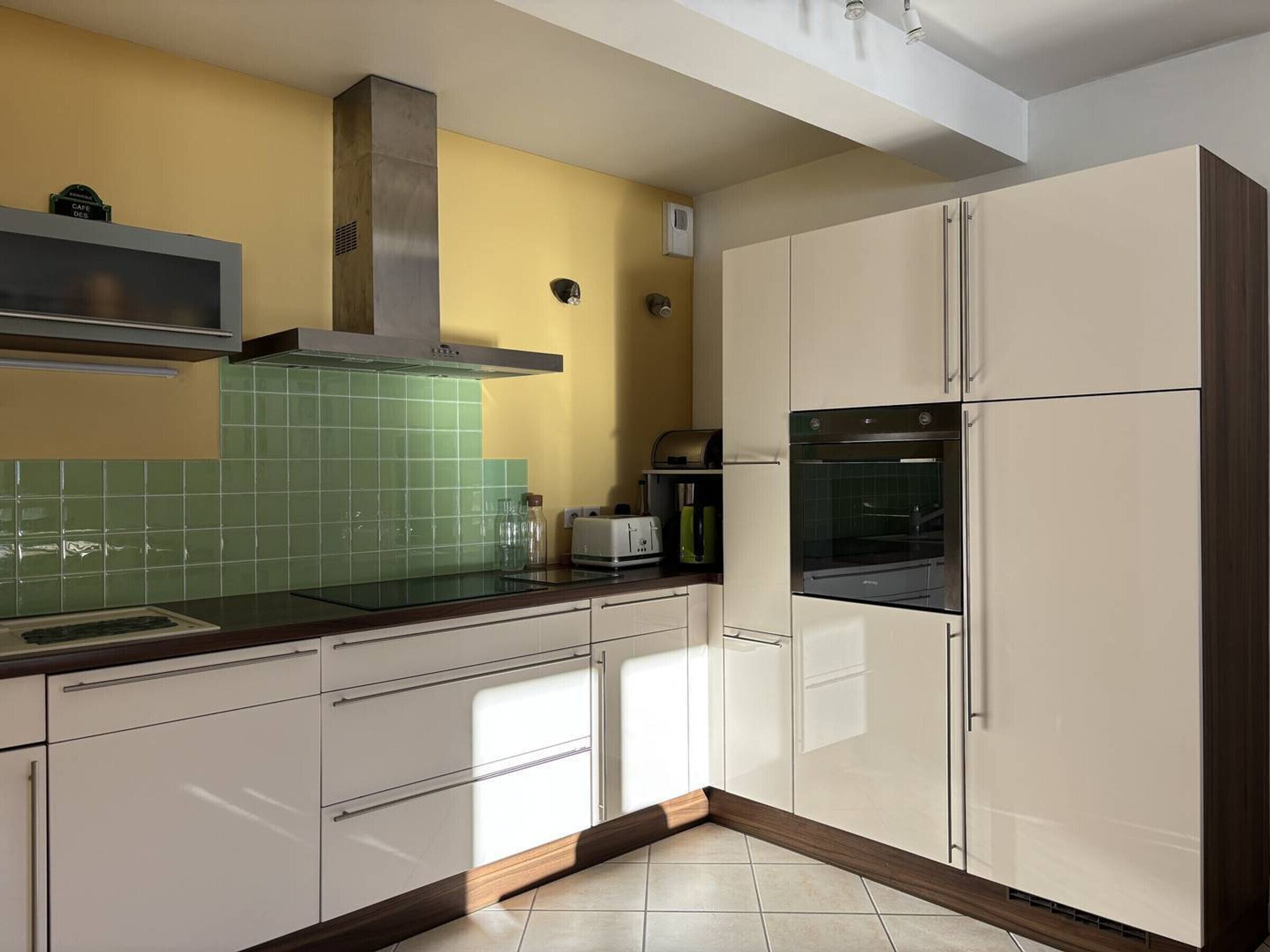 Une cuisine moderne avec des armoires blanches, une hotte de cuisinière en acier inoxydable et un dosseret de carrelage vert.