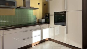 Una cuina moderna amb armaris blancs, una campana extractora d'acer inoxidable i un frontó de rajoles verdes.