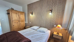 Quarto com cama, guarda-roupa de madeira e mesa de cabeceira com abajur.