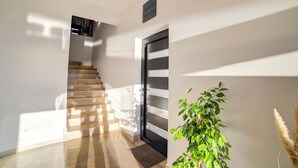 Een modern interieur met een trap, een zwarte deur met glaspanelen en een potplant.