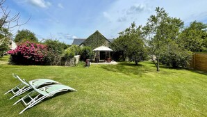 A backyard with a lawn, a covered patio, and a house with a green roof.