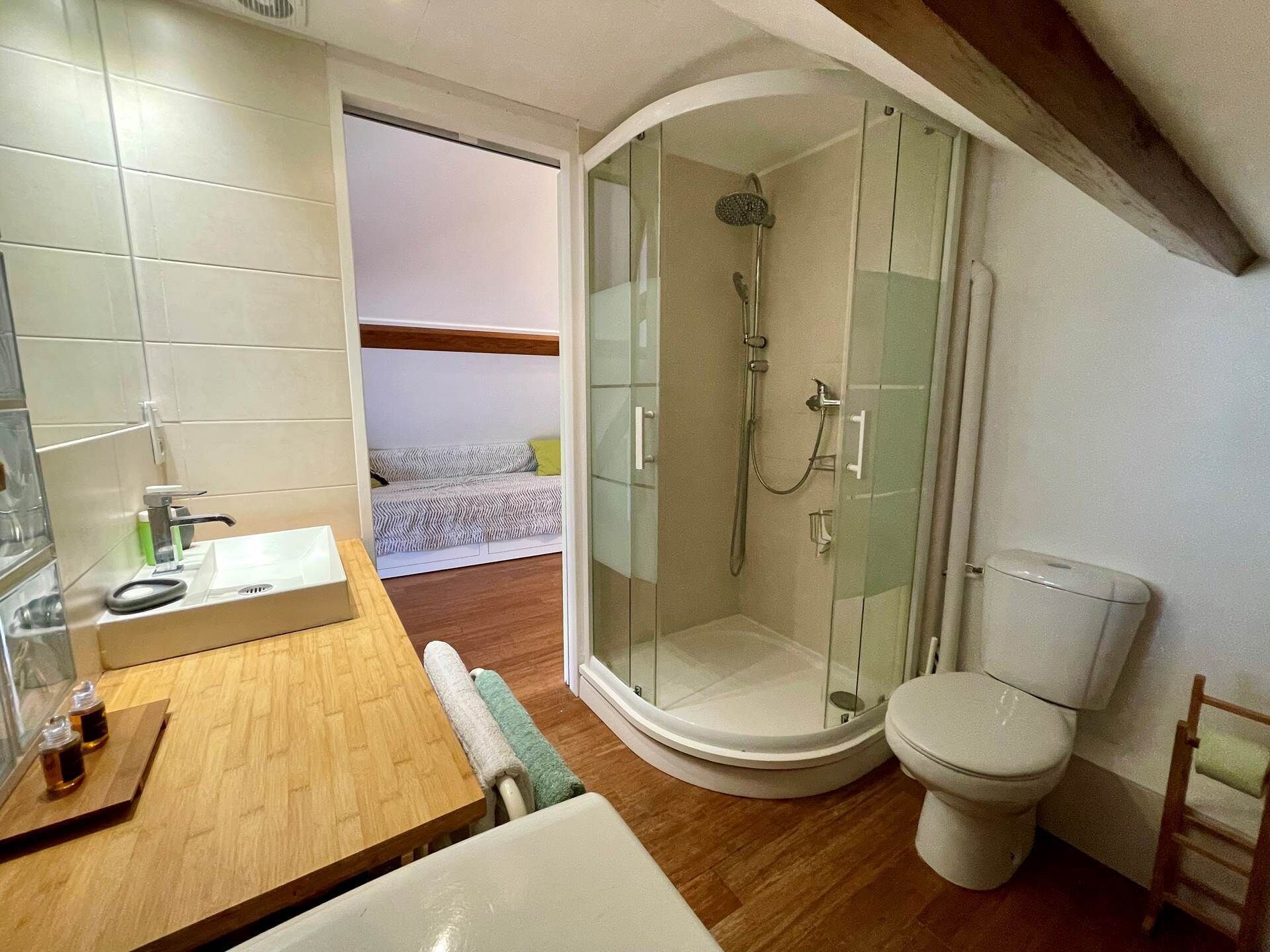Une salle de bain compacte dotée d’une douche à parois de verre, de toilettes et d’un lavabo avec un plan de travail en bois.