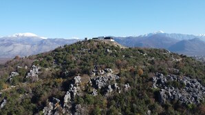 Une montagne surmontée d’un petit bâtiment, entourée d’un paysage rocheux et d’une végétation clairsemée.