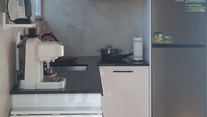 Une cuisine compacte avec un plafond en bois, une cuisinière encastrée, un réfrigérateur blanc et une machine à café.