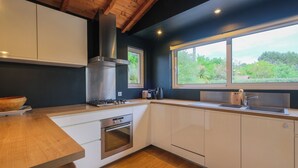 A modern kitchen with white cabinets, a wooden countertop, a built-in oven, a stainless steel range hood, and a large window offering a view of greenery. - Villa Madonne *Pool *Beach *7 sleeps ☀️ (Lège-Cap-Ferret)