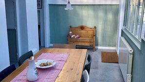 Une terrasse couverte avec une table en bois dressée pour les repas, un banc et un luminaire suspendu.