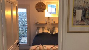Une chambre à coucher avec un lit, une fenêtre, une porte et une étagère fixée au mur.