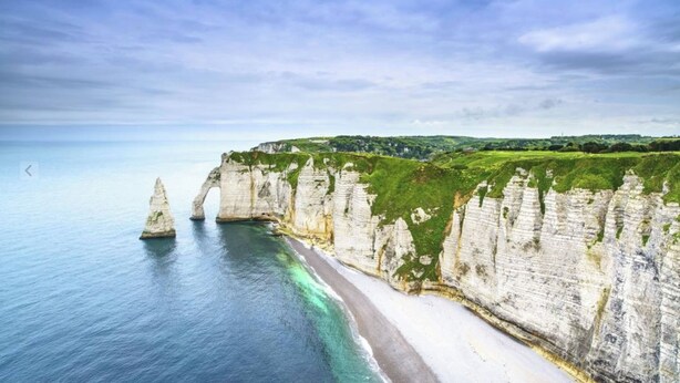 Un paysage côtier avec de hautes falaises blanches, une plage et un ciel dégagé.