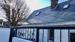 Une véranda dotée d’un toit en tuiles, d’une cheminée en briques et offrant une vue sur le jardin à travers les vitres.