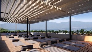 Terraza en la azotea con suelo de madera, colchonetas de yoga y cojines negros, con vistas a un paisaje montañoso.
