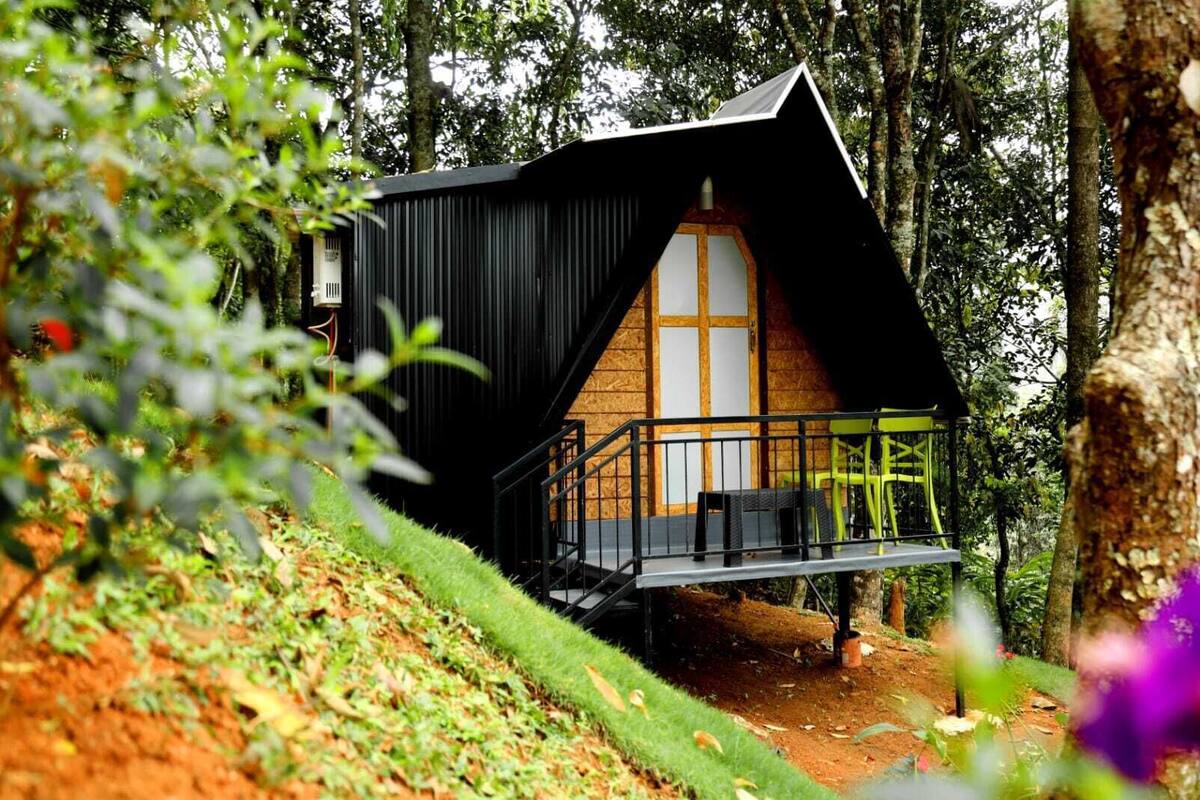 A treehouse with a wooden interior, a balcony with metal railings, and a surrounding forest.