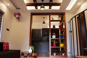 A modern living room with a sofa, a fan, and a wooden shelf with potted plants. - Garden of eden-Thottam (Devikolam)