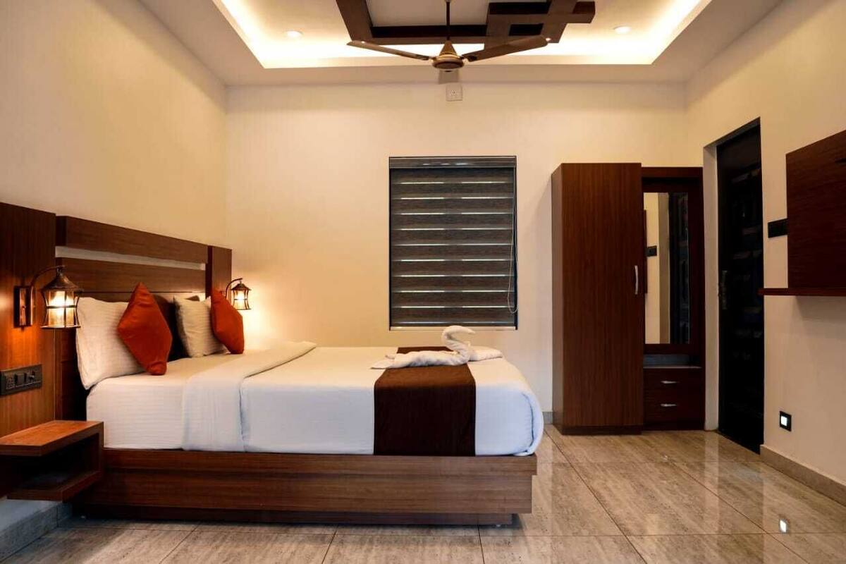 A modern bedroom with a wooden headboard, a large bed with white bedding, a ceiling fan, and a window with blinds.