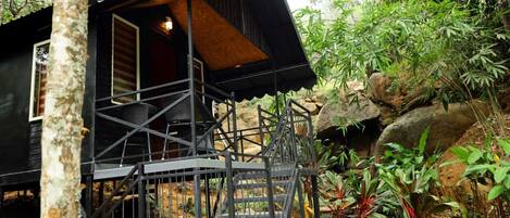 Een boomhuis met een houten interieur, een metalen wenteltrap en een omliggende tuin.