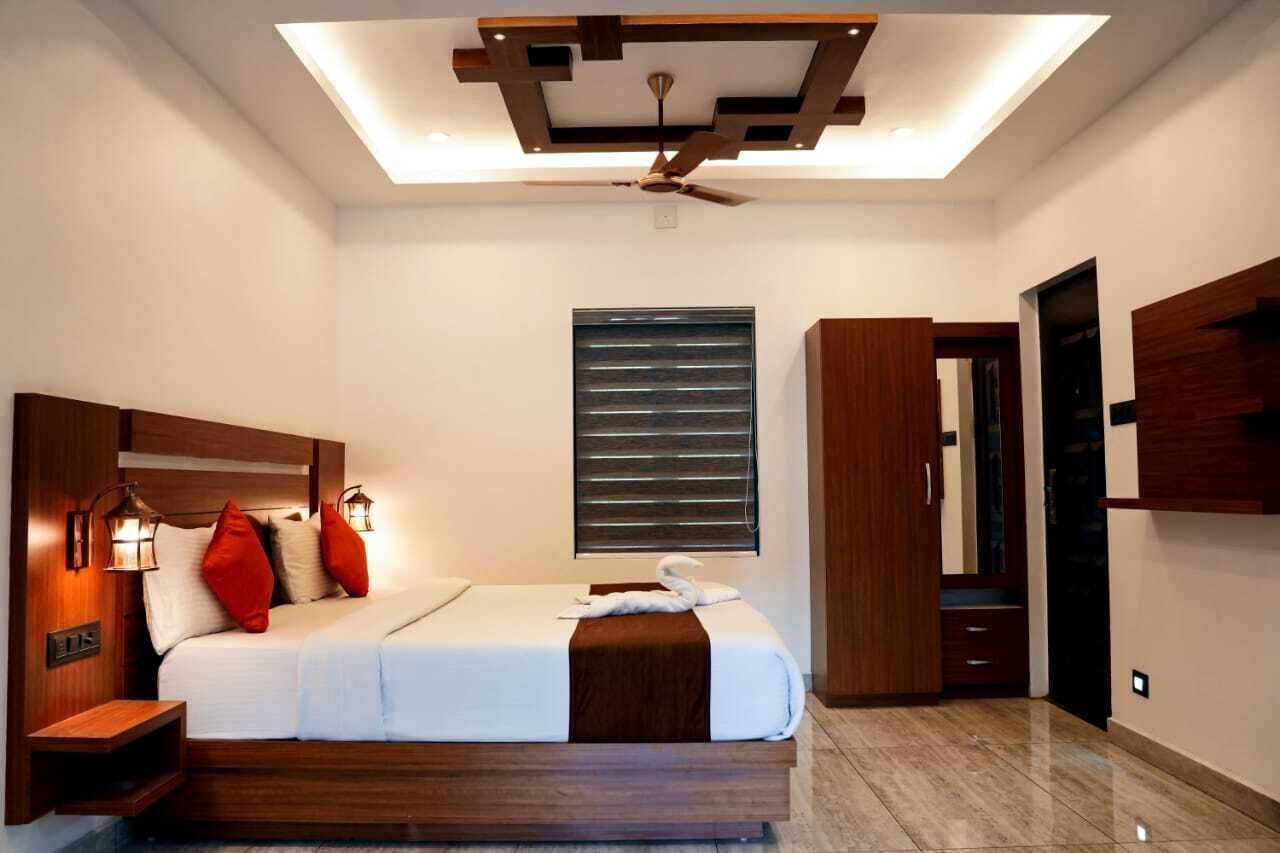 A modern bedroom with a large bed, wooden headboard, bedside lamps, a ceiling fan, and a window with blinds.