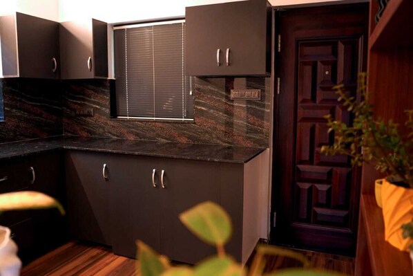Une cuisine moderne avec des meubles de couleur sombre, une fenêtre équipée de stores et une porte décorative en bois.