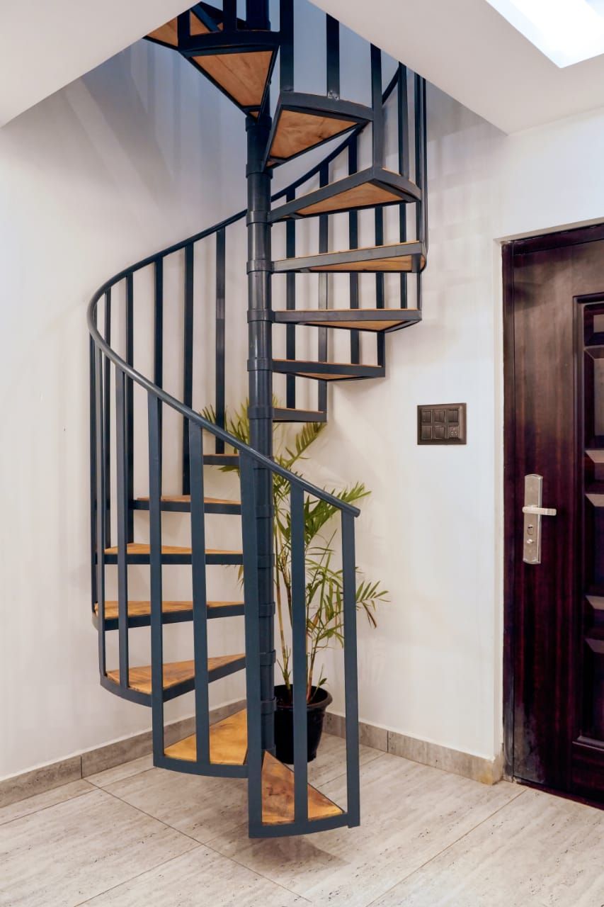 Una escalera de caracol con estructura metálica negra y escalones de madera, que conduce a un piso superior.