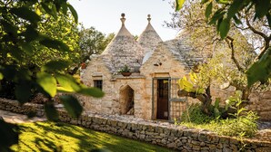 Une charmante maison en pierre avec un toit de chaume, entourée d’un mur de pierre et d’une végétation luxuriante.