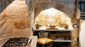 Une cuisine rustique avec un mur en pierre, une cuisinière à gaz, une étagère en bois où sont rangés les ustensiles de cuisine et un luminaire suspendu.