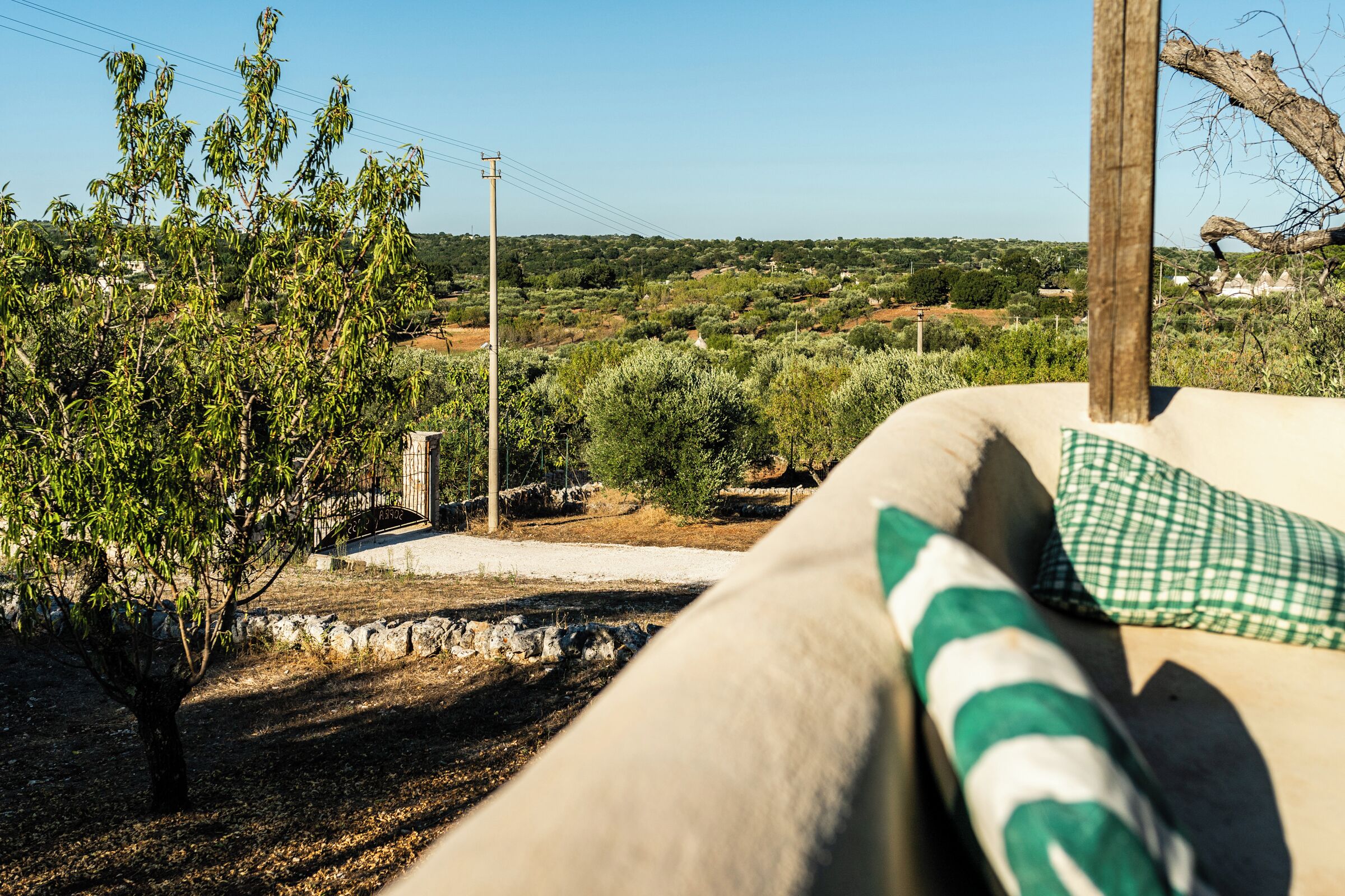 A beige sofa with a green checkered pillow, a view of a rural landscape with trees and a stone wall.