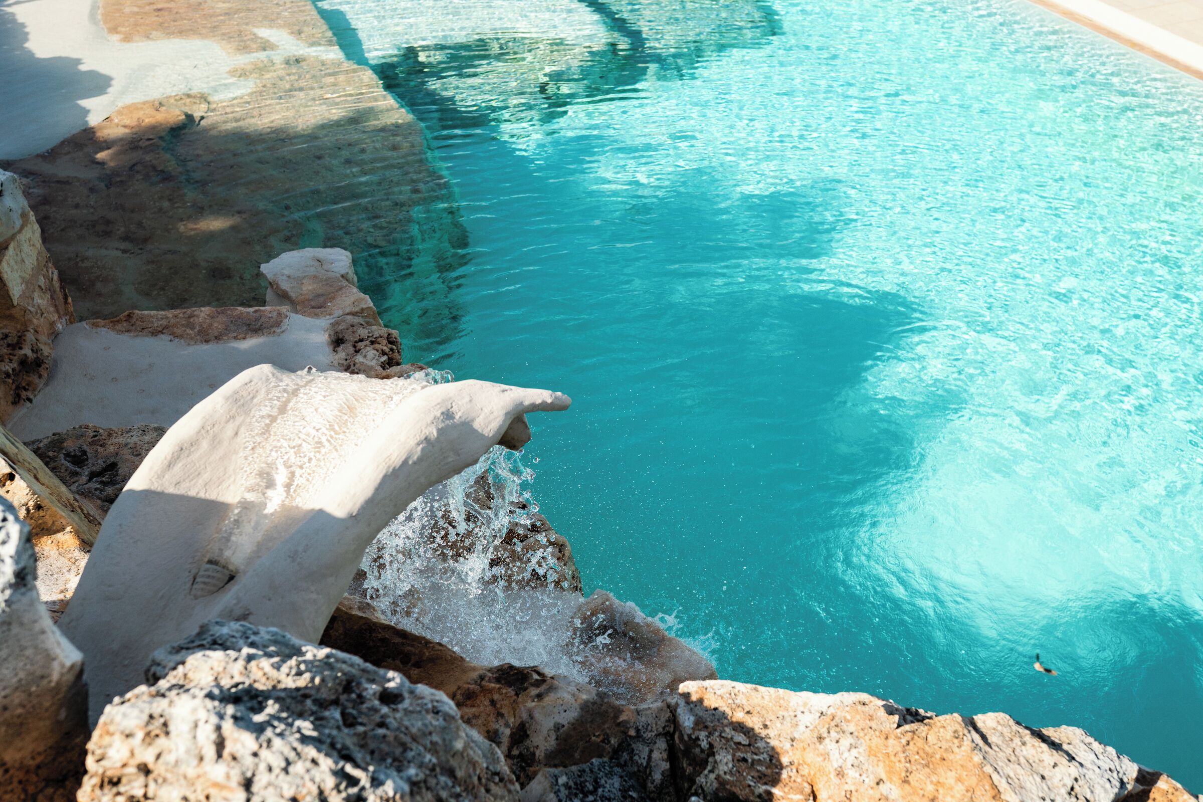 A pool with clear blue water, surrounded by rocky terrain and a sandy beach.