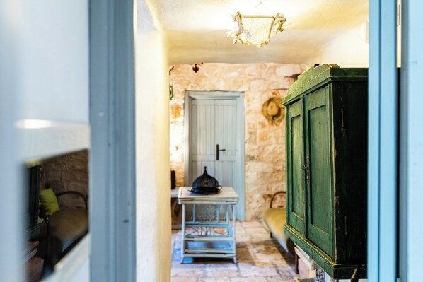 A narrow hallway with a stone wall, a blue door, a green cabinet, and a small table with a decorative object on it.