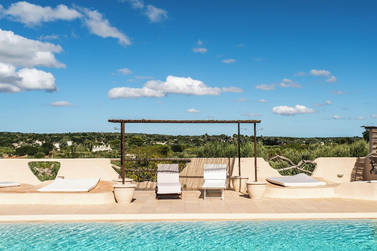 A rooftop pool with lounge chairs and a pergola, overlooking a green landscape.