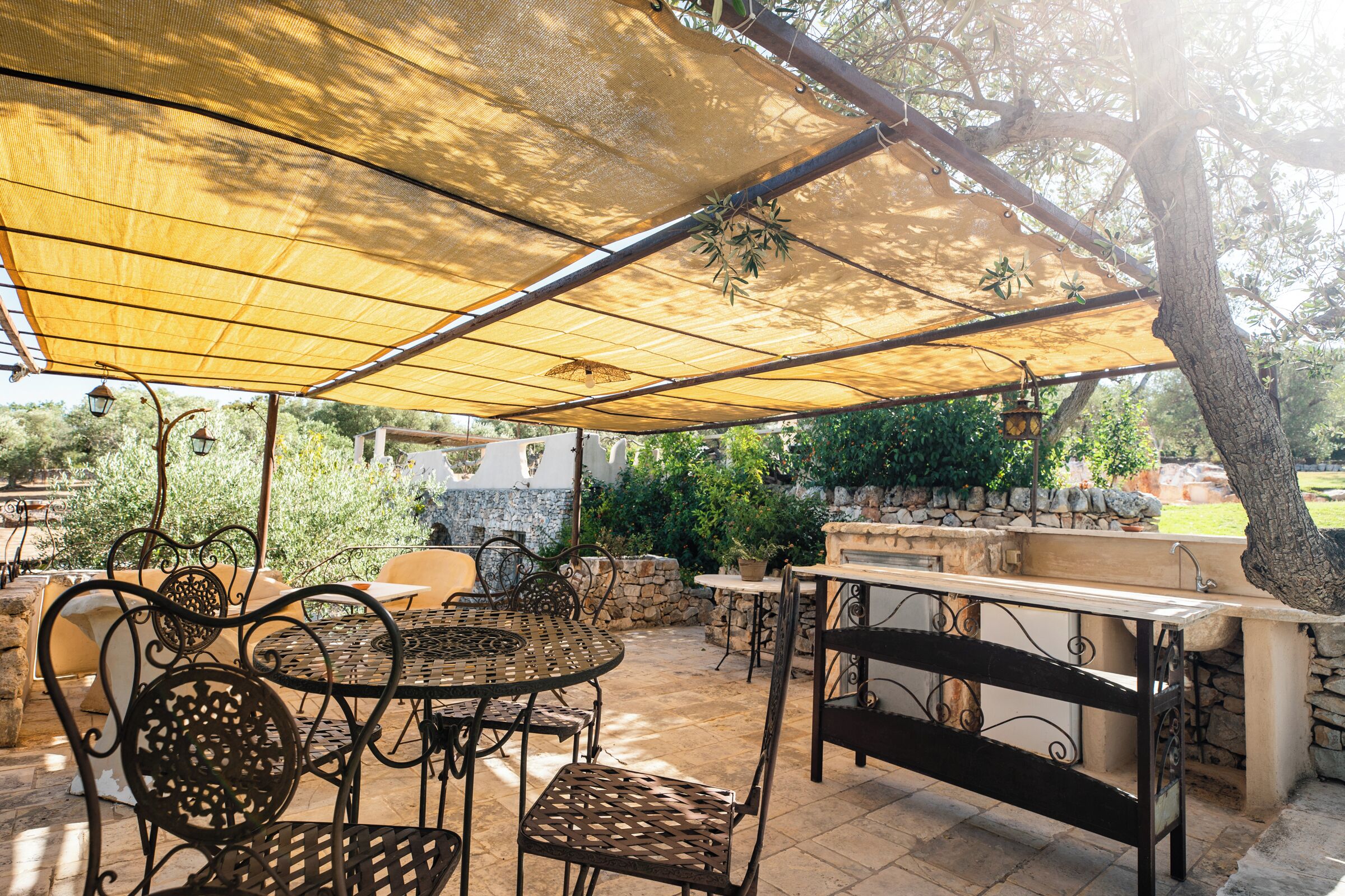 An outdoor patio with metal tables and chairs, a stone bench, and a pergola providing shade.