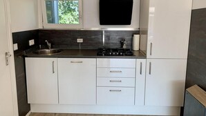 A modern kitchen with white cabinets, a black countertop, a window, and a built-in stove. - Coastal Hideaway Bungalow With Garden (Sint Maartensvlotbrug)