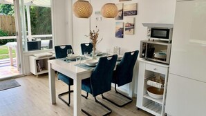 A modern kitchen with white cabinetry, a dining table with blue chairs, and a built-in microwave. - Coastal Hideaway Bungalow With Garden (Sint Maartensvlotbrug)