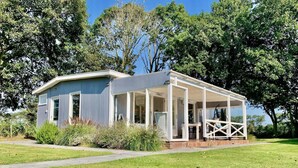 A modern house with a covered porch, a lawn, and trees in the background. - Coastal Hideaway Bungalow With Garden (Sint Maartensvlotbrug)