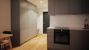 Uma cozinha compacta com armários cinza, forno embutido e uma mesa de jantar de madeira.