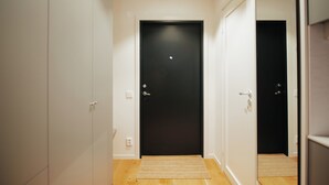 Corredor com uma porta preta, paredes brancas e chão de madeira.