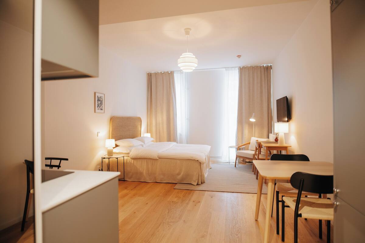 A hotel room with a bed, bedside tables, a desk, chairs, and a television.