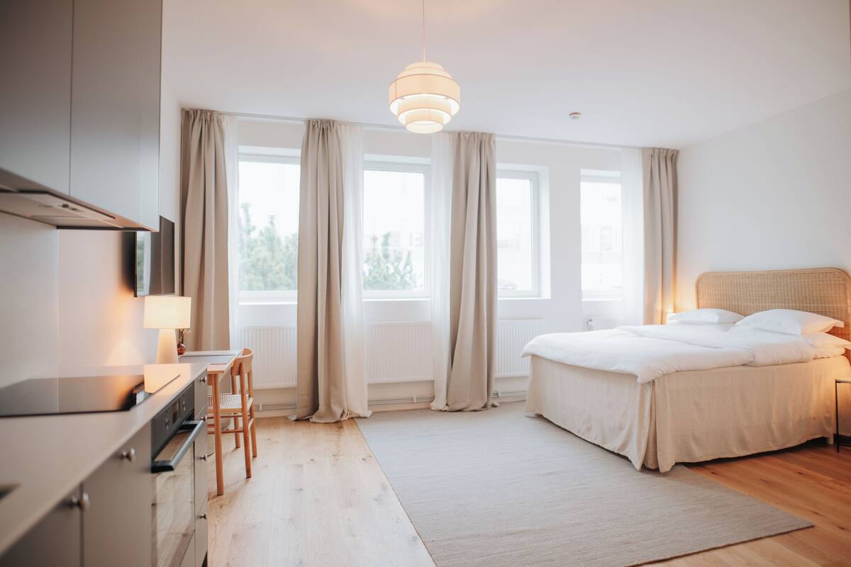 A modern bedroom with a bed, bedside table, lamp, and a view of the outdoors through large windows.