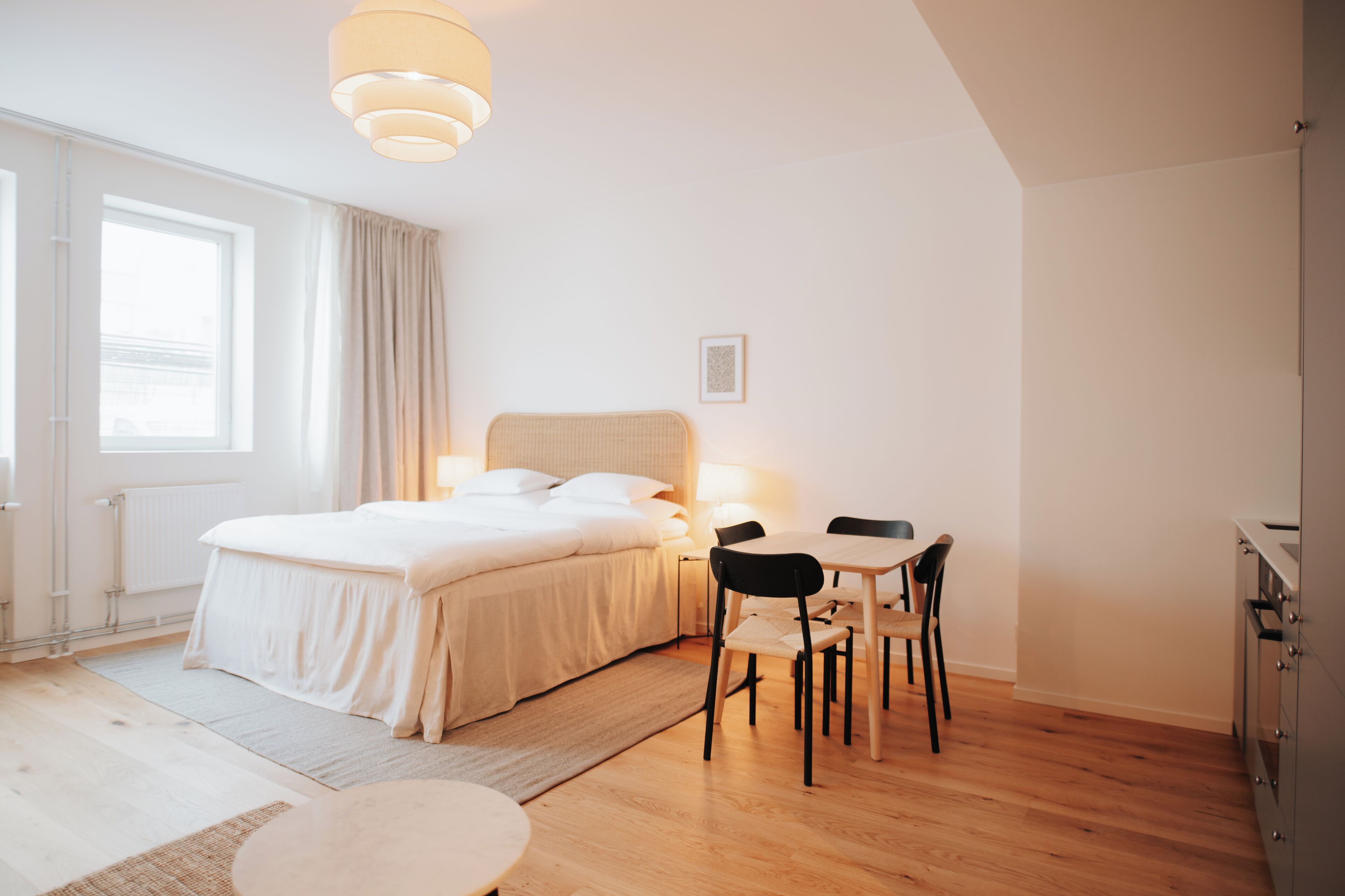 A modern bedroom with a large bed, bedside table, and a small dining area with chairs.